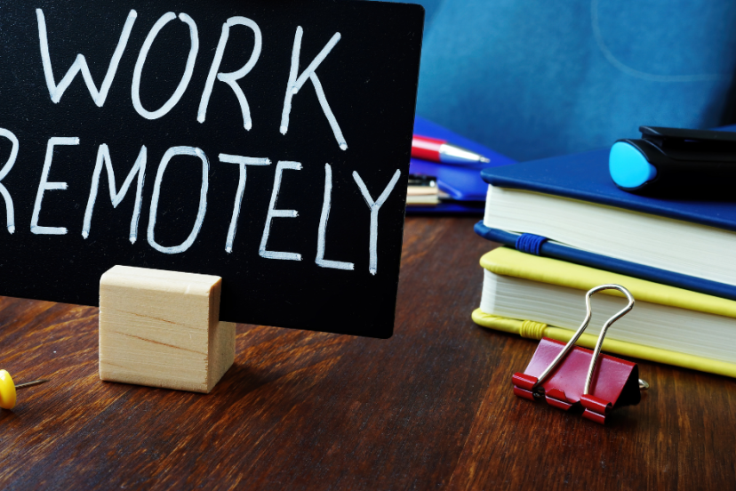 remote job opportunities - image of hardwood desk with a blue and yellow book on top with a black background sign with the phrase "work remotely" written by hand in white letters