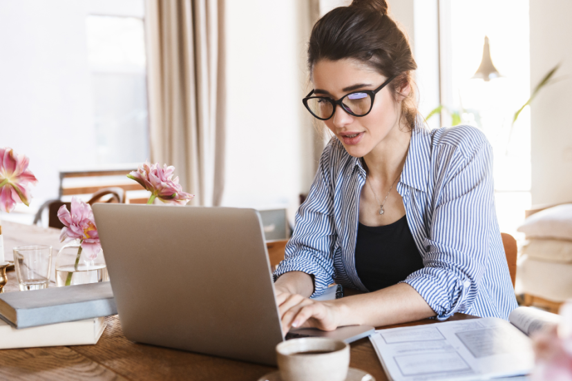 Work-from-home jobs - young Caucasian woman wearing casual clothes and wearing black rimmed eyeglasses while working on her laptop